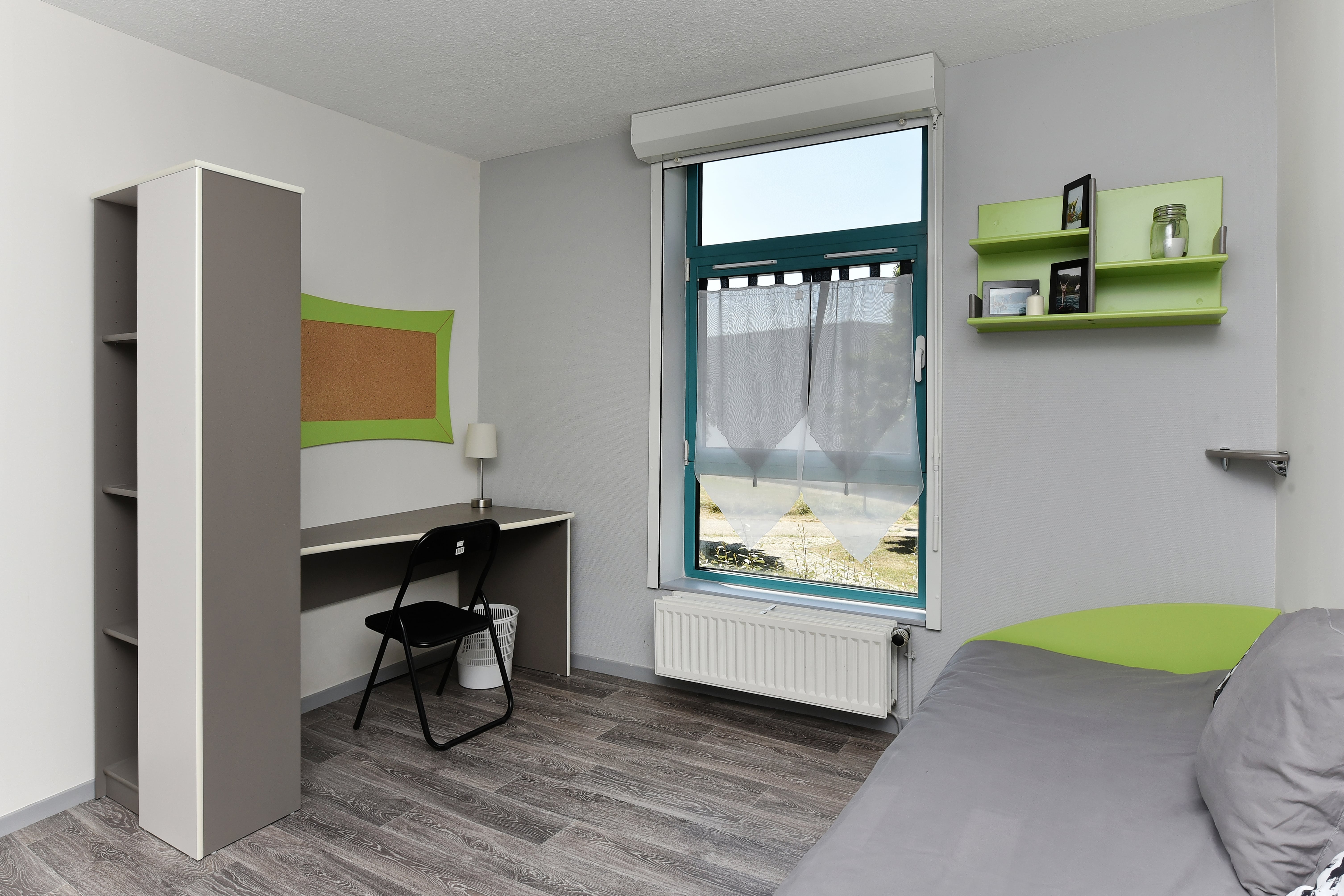 Une chambre étudiant meublée et moderne : un lit 1 place, un bureau, des étagères et une fenêtre donnant sur le parc.