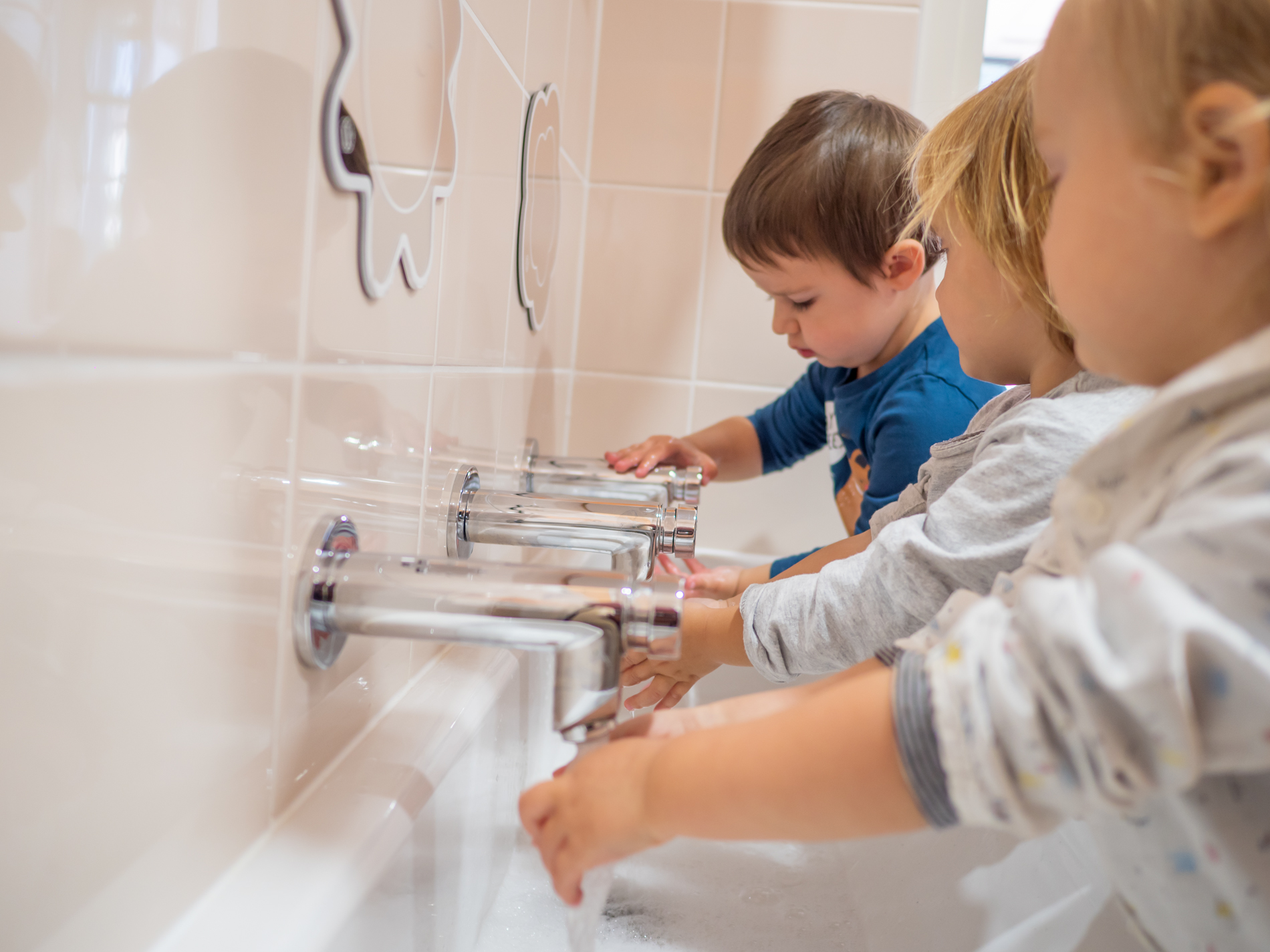 3 enfants se lavent les mains, seuls au lavabo en autonomie. Le lavabo est adapté à leur taille.
