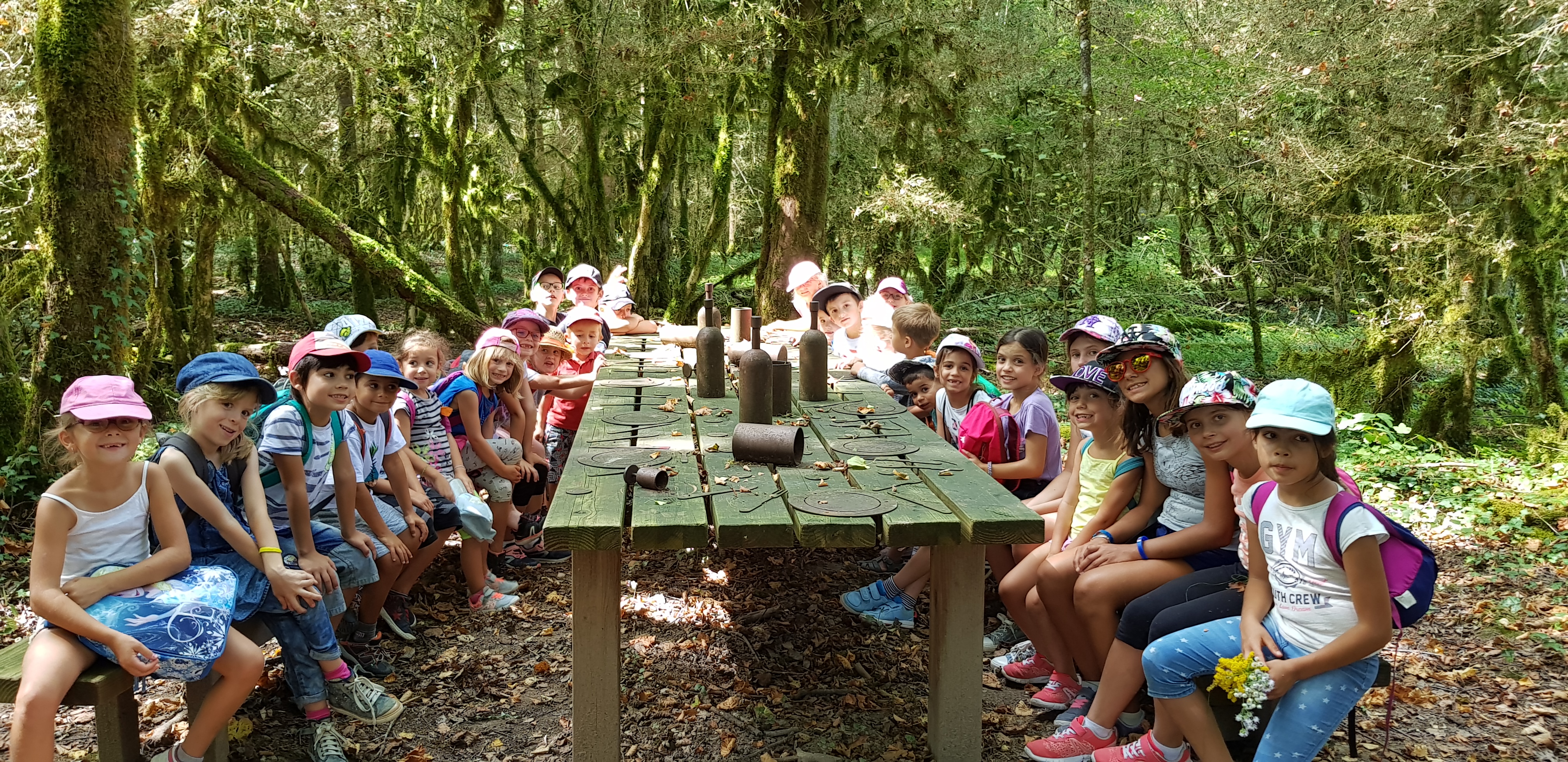 Les enfants de l’accueil de loisirs sont assis autour d’une grande table qui fait partie du parcours conté à Vaux les Saint Claude