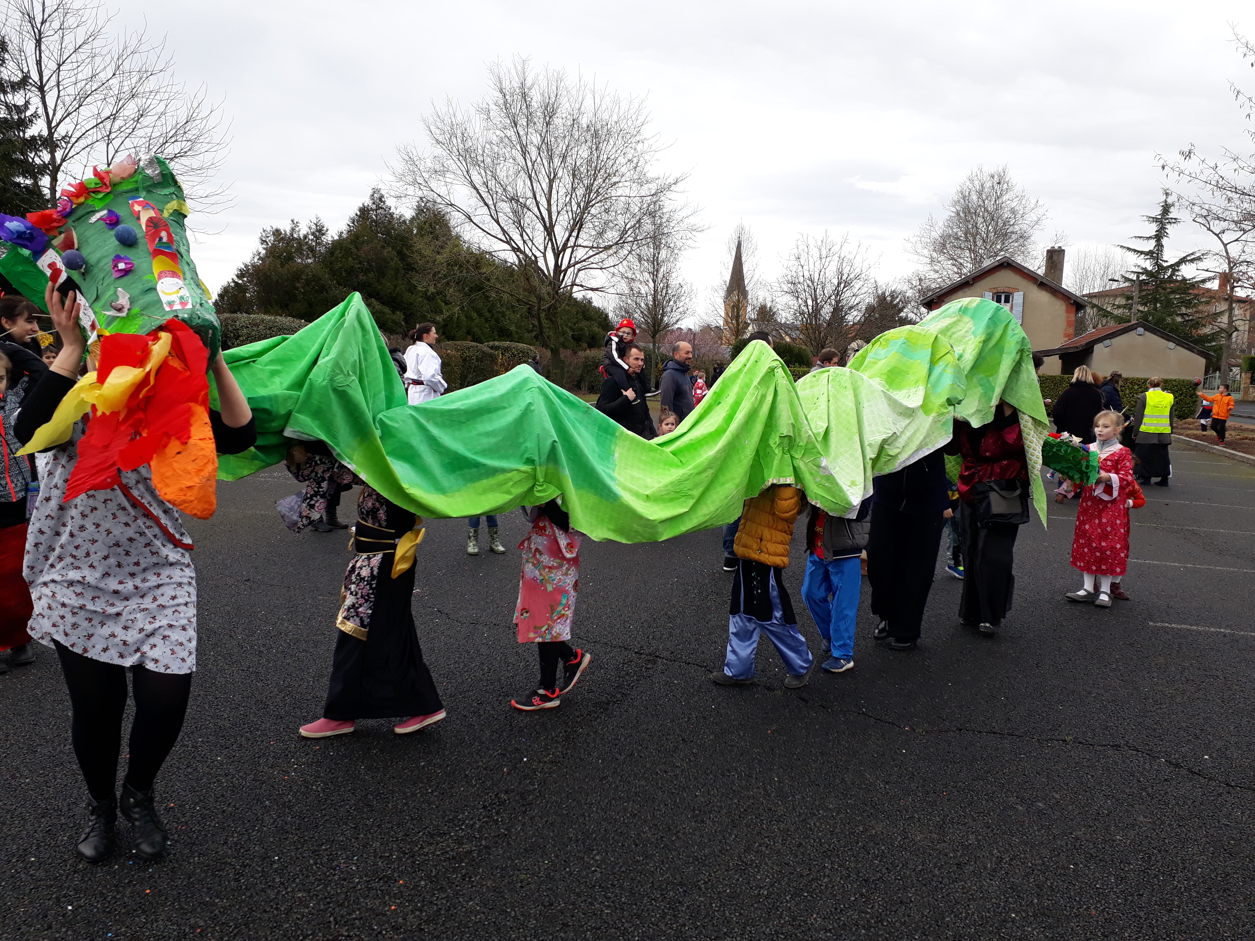 Des enfants portent un draps vert en guise de corps pour le dragon, un adulte porte la tête