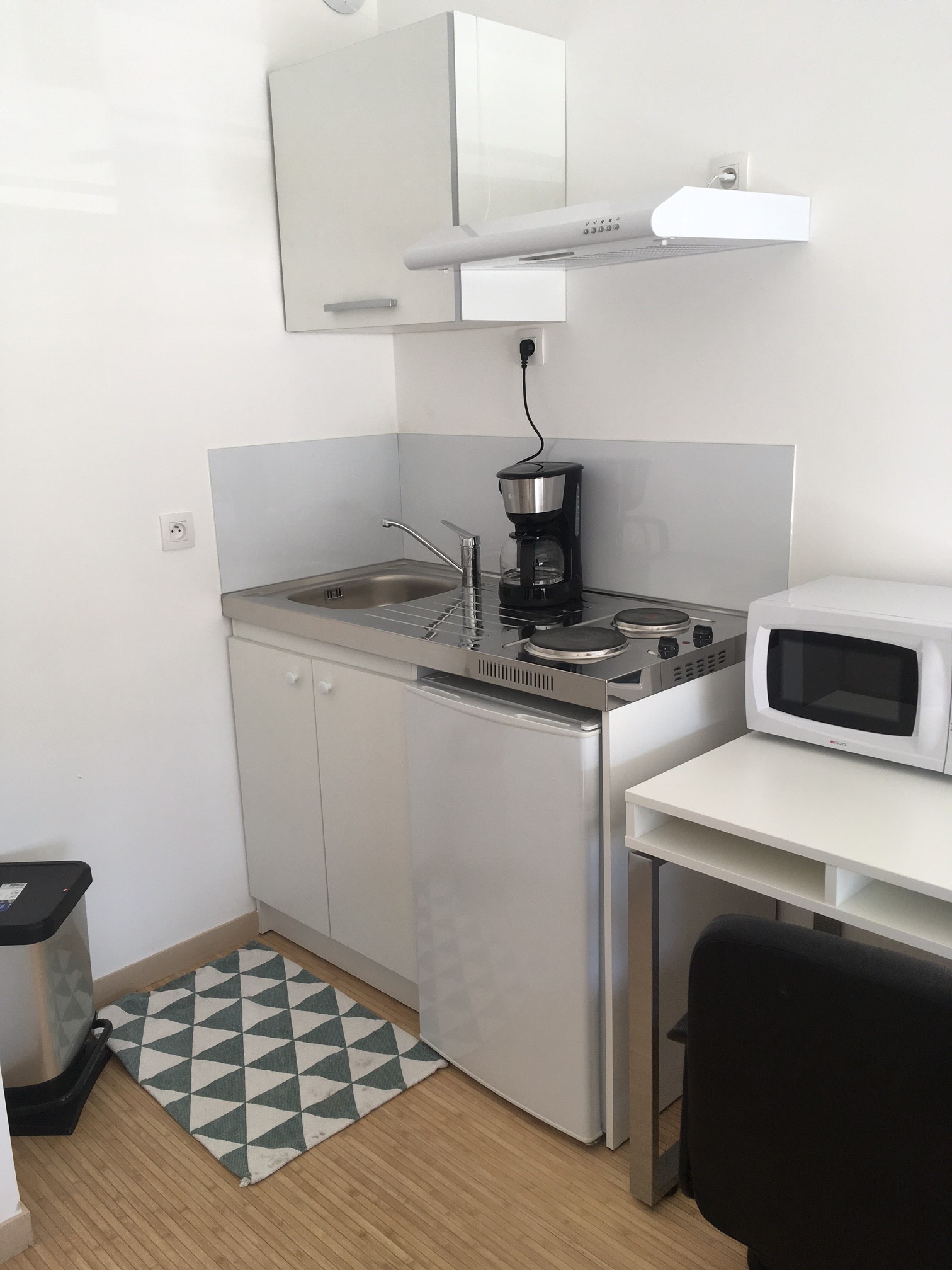 Coin cuisine d&#039;un studio : kitchenette, deux plaques, un mini-frigo, des placards, un micro-onde et une table