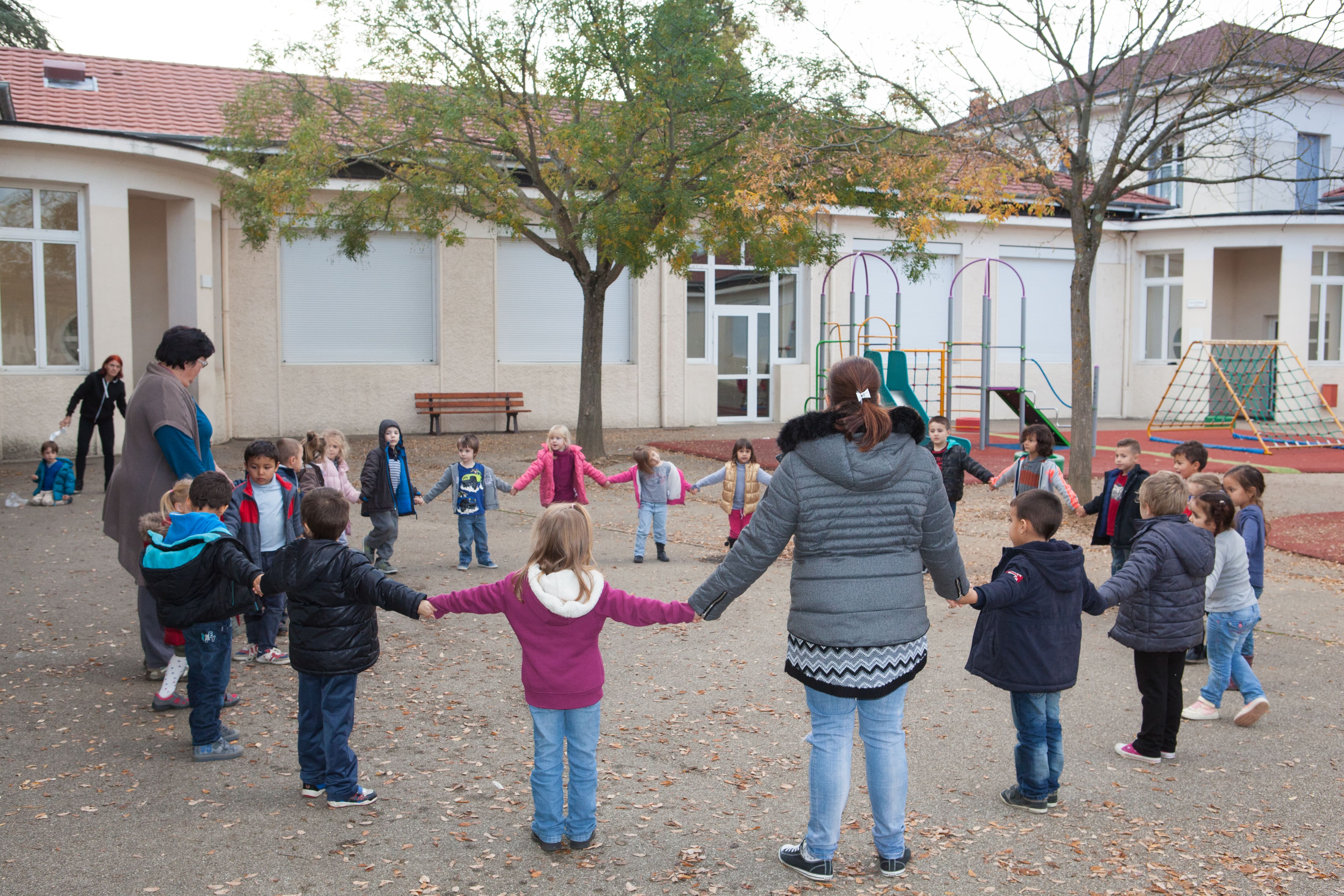 Des enfants et leurs animateurs faisant une ronde dans la cour