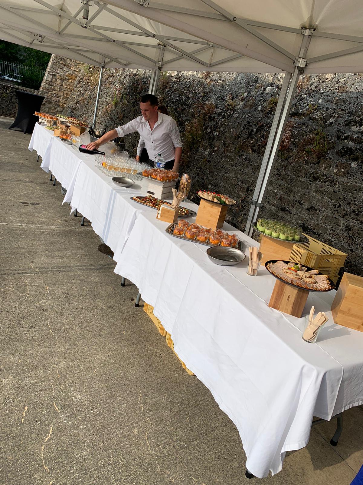 Le buffet est installé sur des tables, en extérieur sous un barnum. Un serveur finalise la mise en place.