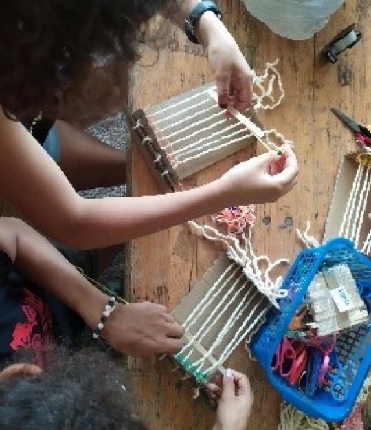 Atelier pour le programme d'été : deux personnes fabriquent un objet sur des métiers à tisser (vue du haut)