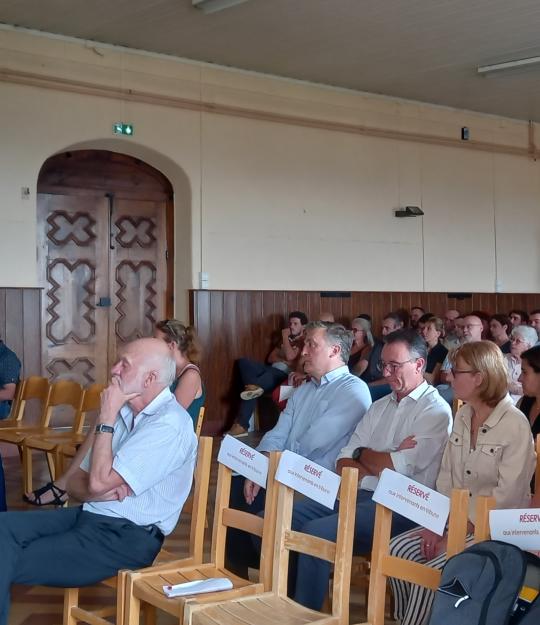 Le public de l'AG 2023 d'Alfa3a était constitué de partenaires institutionnels et de salariés. Vue de face : dans le château, les invités assistent à l'assemblée générale, assis sur des chaises en bois disposées en lignes
