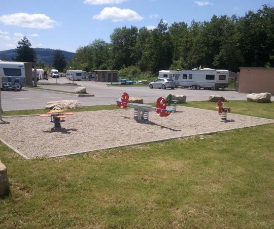 Aire de passage pour les gens du voyage, on voit des jeux aménagés à l'extérieur et des caravanes garées sur un grand parking.