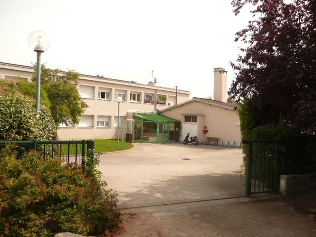 Vue du bâtiment à 1 étage depuis l'entrée du portail, on voit un chemin et des arbres