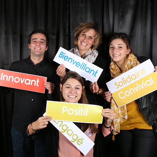 Des salariés souriants tenant des pancartes où sont écrites les valeurs d'alfa3a : bienveillant, innovant, positif, engagé, solidaire, convivial...